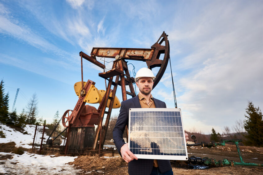Businessman standing with a solar panel in front of an oil rig
