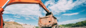 Industrial working excavator loading dumper truck during earthworks, highway construction site and soil transportation