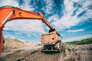 Industrial working excavator loading dumper truck during earthworks, highway construction site and soil transportation