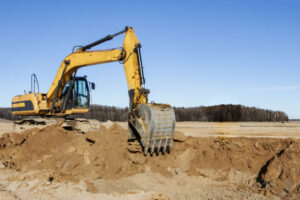 A powerful caterpillar excavator digs the ground against the blue sky. Earthworks with heavy equipment at the construction site