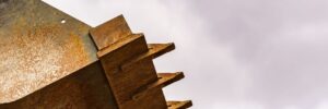 Close-up of a rusted heavy equipment bucket blade with pointed metal teeth against a cloudy sky.
